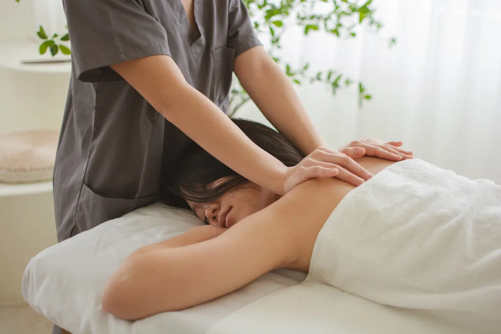A woman lying face down on a massage table, receiving a back massage from a therapist.
